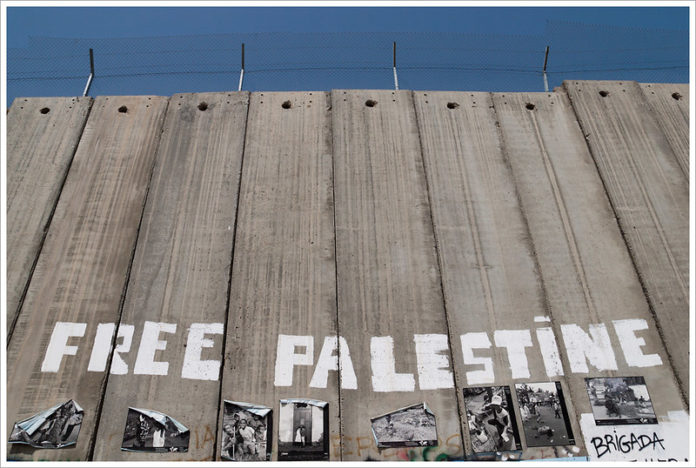 A photo of the immeasurably high apartheid wall with the words 'FREE PALESTINE' painted on it.