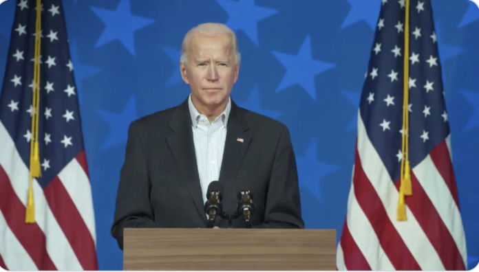 Joe Biden stands in front of two US flags