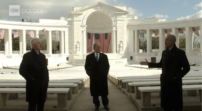 Former US presidents Clinton, Bush and Obama stand socially distanced speaking in front of a white amphitheater.