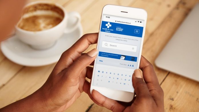 A phone open on the NHS app is held in two hands while a cup of coffee is in the background.