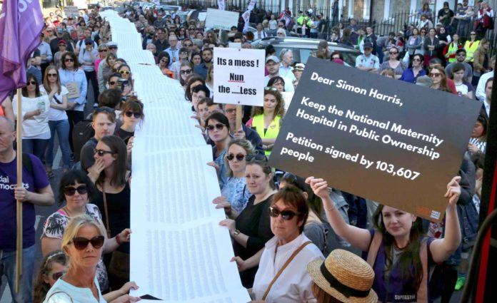 A packed street at a demo as people hold a long line of signatures