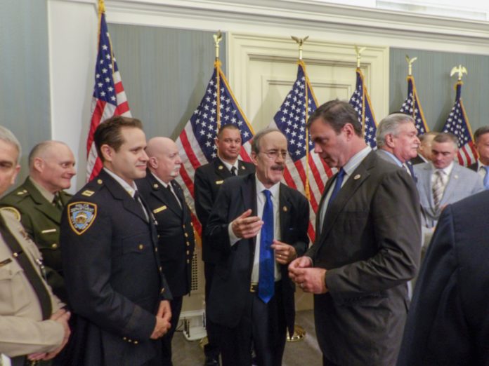 Eliot Engels speaks to a number of men in police uniforms as they stand in front of a number of US flags