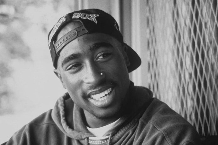 A black and white photo of Tupac Shakur smiling.