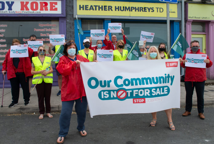 A dozen protesters in masks stand in front of a building that says 