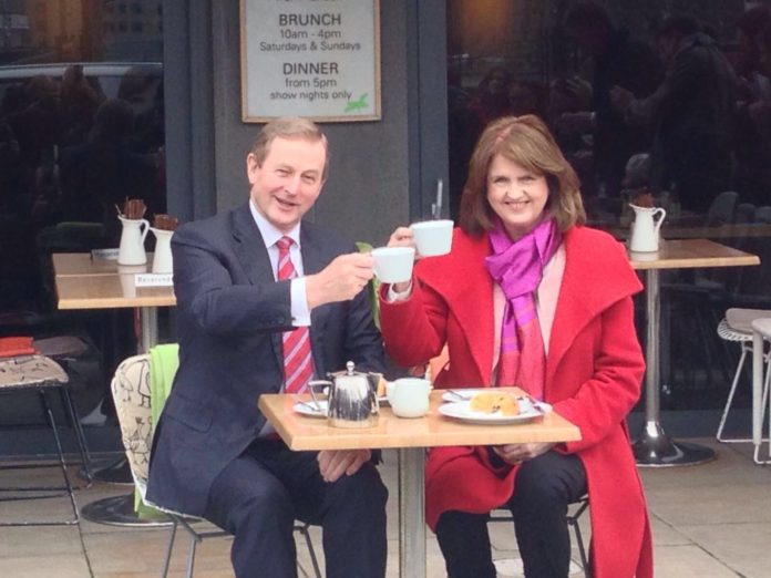 Enda Kenny and Joan Burton smile and hold up tea cups